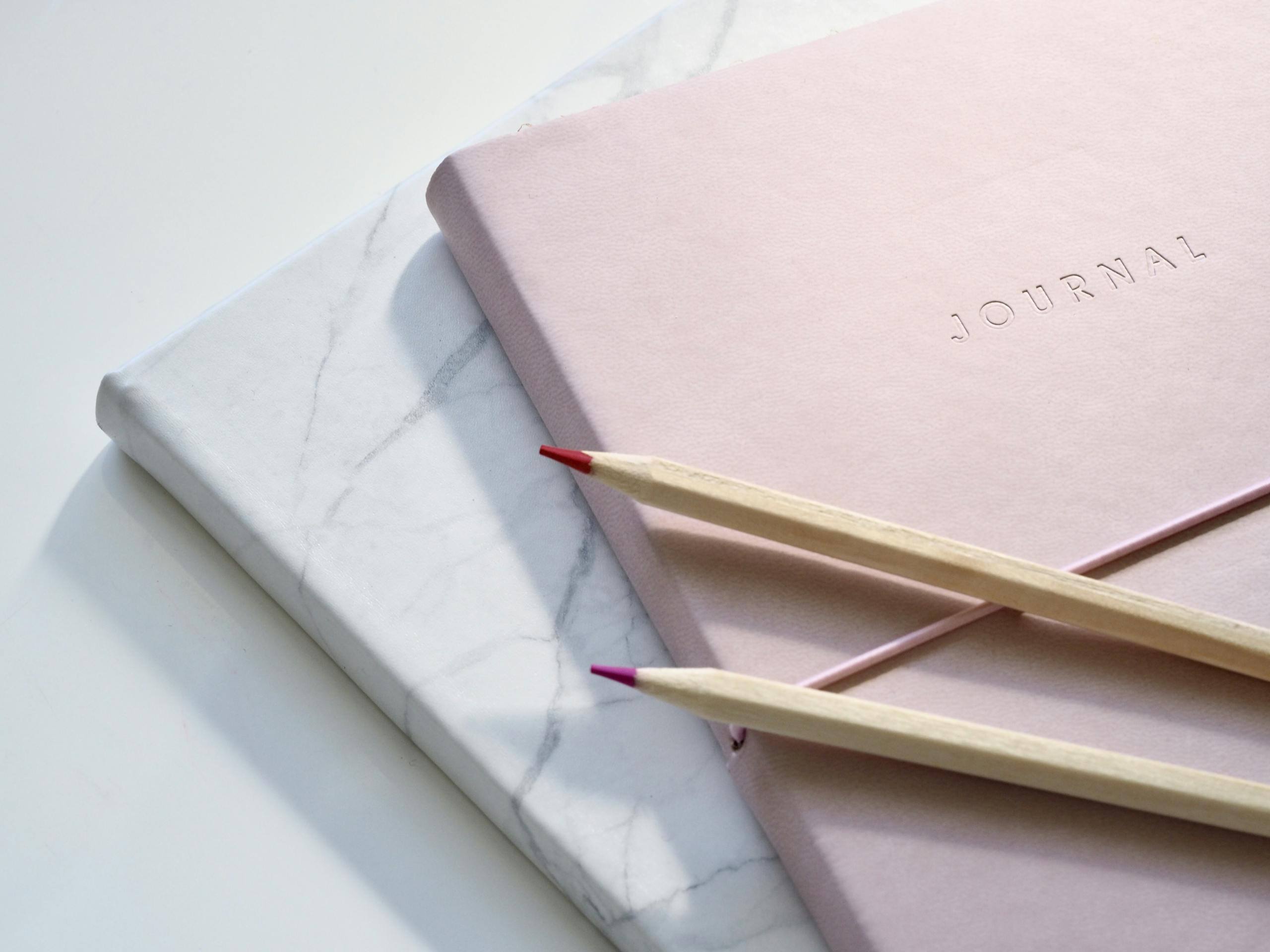 Close-up of a pink journal with pencils on a marble top. Perfect for note-taking or planning.
